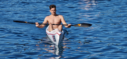 Ein junger Mann paddelt im Kajak auf ruhigem Wasser.