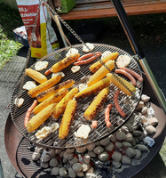 Gegrillter Mais und Würstchen auf einem Grillrost über Kohlen.