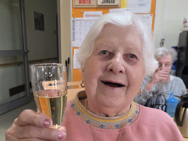 Ältere Frau hebt ein Glas und lächelt.