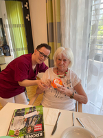 Pflegekraft hilft einer älteren Frau beim Halten eines bunten Objekts.