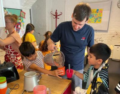 Gruppe von Kindern schüttet Smoothie in Becher, Mann hält Krug