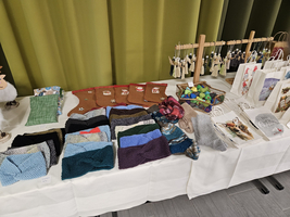 Bunte Handarbeiten und Strickwaren sind auf einem Tisch ausgestellt.