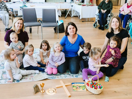 Eine Gruppe von Kindern und Erwachsenen sitzt auf einem Teppich mit Spielzeug.