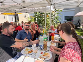 Gruppe von Menschen genießt gemeinsam ein Essen unter einem Pavillon im Freien.