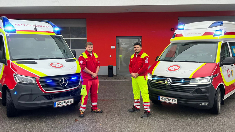 Zwei Rettungskräfte stehen neben einem Rettungswagen vor der Rettungsstelle.