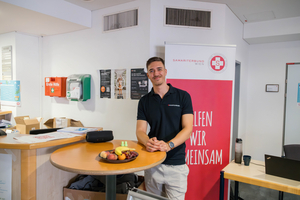 Ein Mann steht lächelnd vor einem Tisch mit Obst und einem Werbebanner.