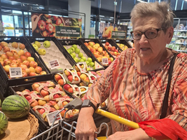 Ältere Frau mit Einkaufwagen in einem Obst- und Gemüseladen.