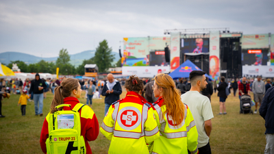 Drei Sanitäterinnen beobachten ein Festival mit vielen Besuchern im Hintergrund.