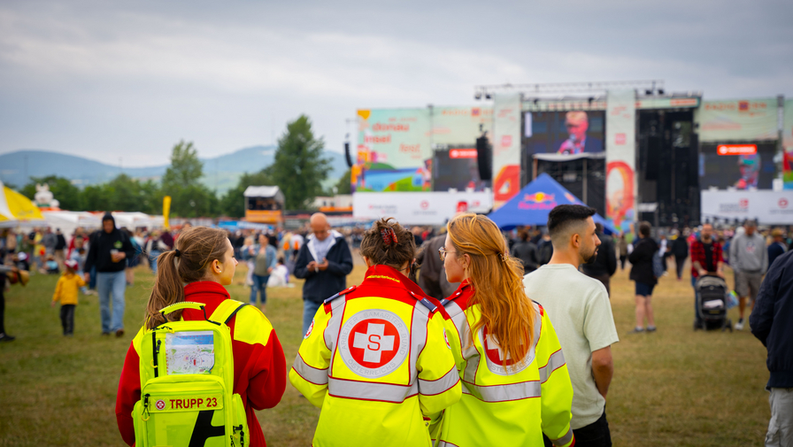 Drei Sanitäterinnen beobachten ein Festival mit vielen Besuchern im Hintergrund.