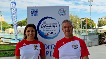 Zwei Personen in Sportbekleidung vor einem Banner der Weltmeisterschaft im Rettungsschwimmen.