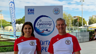 Zwei Personen in Sportbekleidung vor einem Banner der Weltmeisterschaft im Rettungsschwimmen.