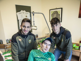 Drei Fußballspieler posieren mit einem Fan im Rollstuhl und einem signierten Ball.