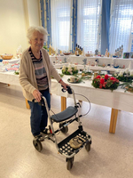 Eine ältere Frau mit Rollator lächelt in einem festlich dekorierten Raum.