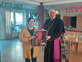 Eine Frau und ein Geistlicher halten zusammen ein Bild.