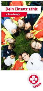 Gruppe von Kindern in bunten Jacken liegt im Kreis auf dem Rasen.