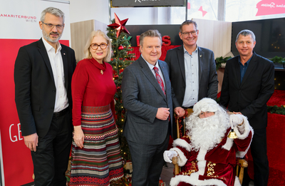 Fünf Personen stehen um einen Weihnachtsmann vor einem festlich geschmückten Baum.