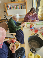 Drei Personen schälen Äpfel am Tisch in einer hellen Umgebung.