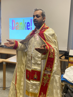 Ein Mann in traditioneller Kleidung steht und spricht mit ausgestreckten Händen.