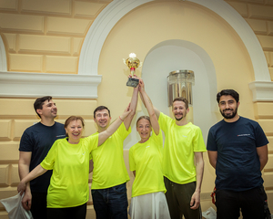 Gruppenfoto Sieger:innen Tischtennisturnier mit Pokal, halten in gemeinsam in die Höhe, tragen alle neongelbe T-Shirts, links und rechts zwei Betreuer mit blauen Samariterbund Wien Polo-Shirts