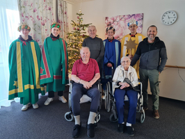 Gruppenfoto von Senioren und verkleideten Personen vor einem geschmückten Weihnachtsbaum.