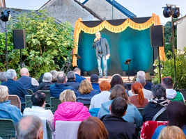 Ein Stand-up-Komiker tritt vor einem Publikum im Freien auf.