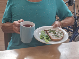 Eine ältere Frau hält eine Tasse und einen Teller mit belegtem Brot.