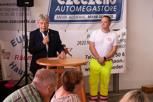 Mann spricht am Mikrofon, im Hintergrund eine Person in Arbeitskleidung.