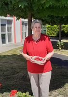Eine ältere Frau steht im Freien und hält eine Schüssel mit Erdbeeren.