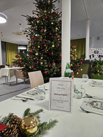 Tisch gedeckt für Weihnachtsfeier mit Weihnachtsbaum im Hintergrund.