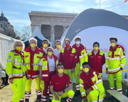 Gruppenbild Sanitäterinnen in Uniform, draußen, Sonnenschein, alle tragen gelbe FFP2-Masken