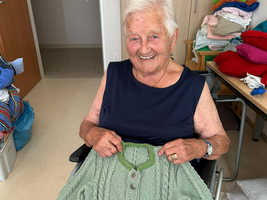 Eine ältere Frau sitzt im Rollstuhl und hält einen grünen Strickpullover.