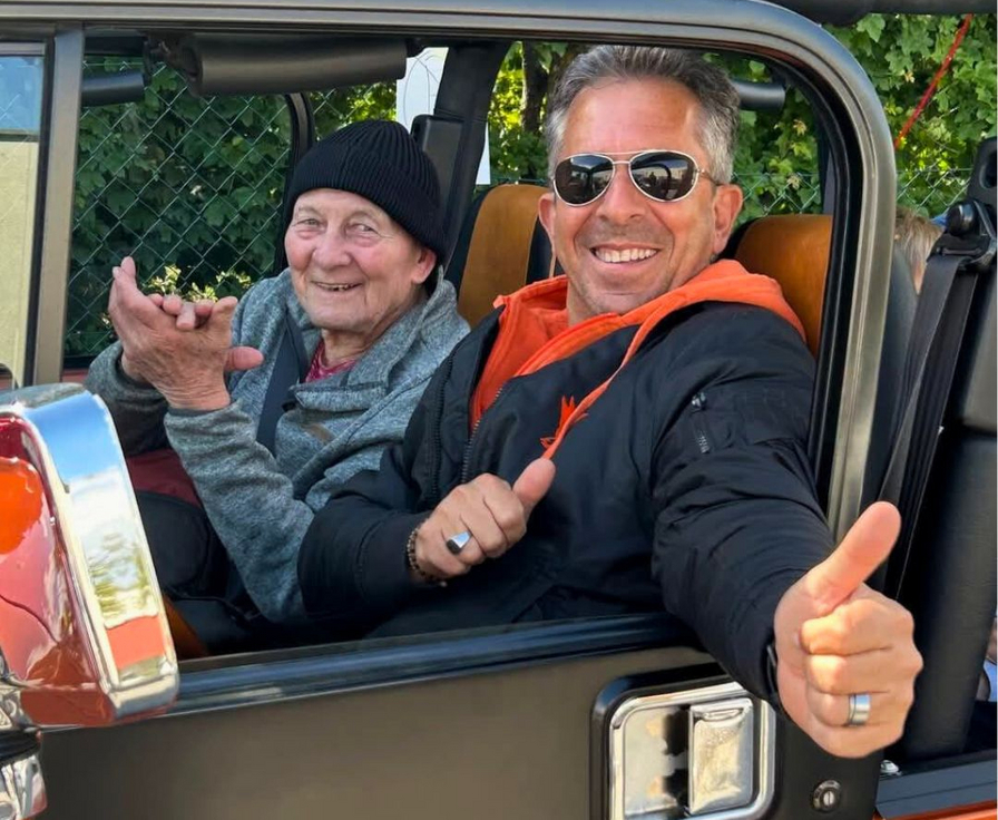 Zwei lächelnde Personen sitzen in einem Auto und zeigen den Daumen hoch.