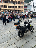 Eine Menschenmenge steht auf einem Platz, während ein Motorrad im Vordergrund parkt.