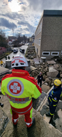 Rettungskräfte inspizieren eine Unglücksstelle mit Trümmern und Einsatzfahrzeugen.