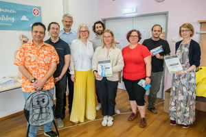 Gruppe von Menschen bei einer Veranstaltung, halten Urkunden und Broschüren in die Kamera.