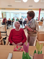 Zwei Frauen unterhalten sich, eine überreicht der anderen ein Geschenk.