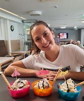 Eine Frau lächelt neben bunten Eisschalen mit Schlagsahne und kleinen Schirmchen.