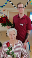 Ein junger Mann gibt einer älteren Frau eine Rose und lächelt.