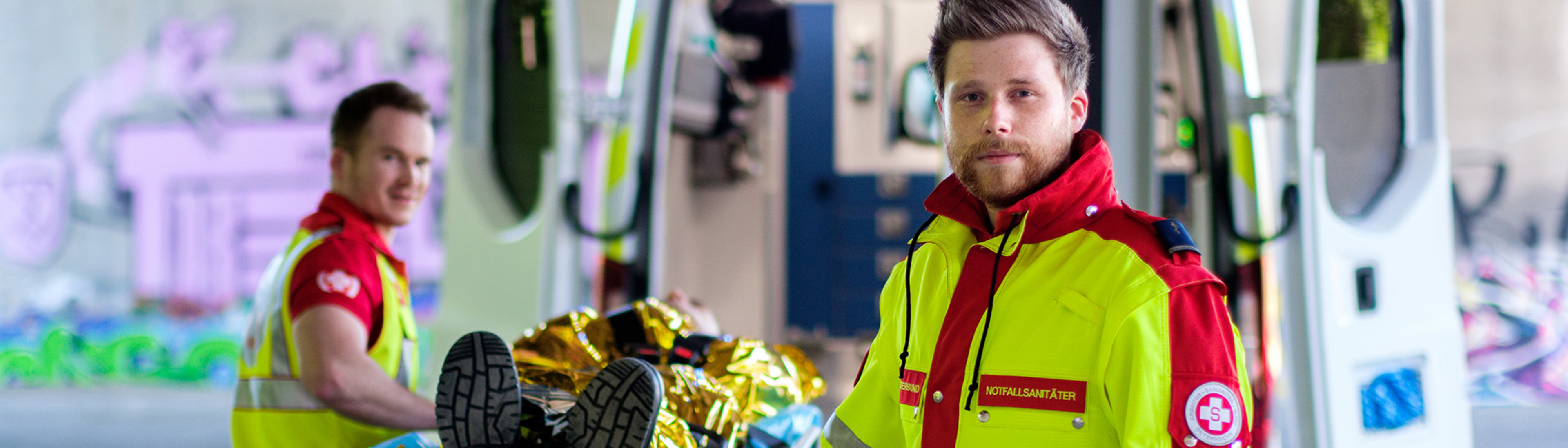 Rettungssanitäter mit Verletztem auf Trage vor Rettungsauto