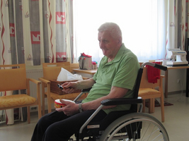 Ein älterer Mann sitzt im Rollstuhl und hält eine Schale in der Hand.