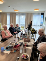Eine Gruppe älterer Frauen sitzt an einem Tisch mit einer Torte und Blumen.