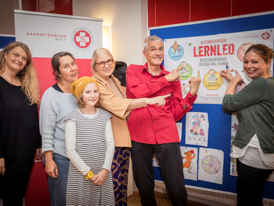 Susanne Drapalik, Marco Simsa, Birgit Greifeneder und einige der LernLEO Kids freuen sich über das tolle Angebot im LernLEO. Sie stehen beisammen und zeigen auf eine Schautafel fürs LernLEO.