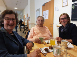 Drei Frauen sitzen an einem Tisch und genießen Getränke und Kuchen.