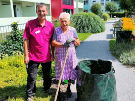Zwei Personen lächeln, während sie im Garten mit einer Schaufel arbeiten.