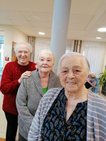 Drei ältere Frauen lächeln herzlich in einem Aufenthaltsraum.