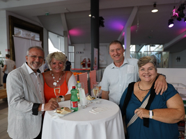 Vier Menschen stehen an einem Stehtisch mit Getränken und Snacks.