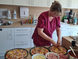 Eine Person belegt mehrere Pizzen mit verschiedenen Zutaten in einer Küche.