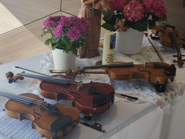 Auf einem Tisch liegen mehrere Geigen mit Notenblättern und Blumenarrangements.