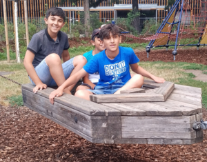 drei Kinder sitzen in Boot aus Holz, Spielplatz