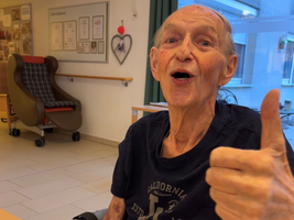 Ein älterer Mann lächelt und gibt einen Daumen nach oben über seinem Essen.